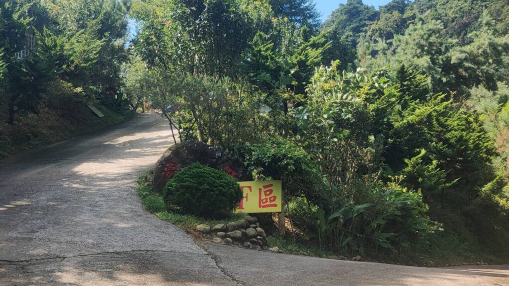 苗栗夢之谷露營區內的一處林蔭岔路，指標顯示右側通往 F 區草地區，左側小徑則可前往營本部，四周環繞的綠樹展現了適合親子露營與三代同遊的自然環境。
