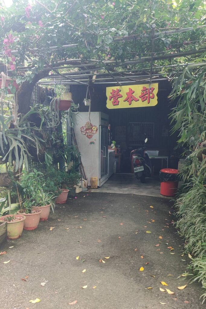 苗栗夢之谷露營區的營本部外觀，掛著黃色招牌，入口處綠意盎然，營主在此提供親切服務與公共冰箱等設施。